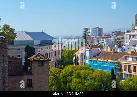 Malaga, Spagna - storiche mura di pietra e torri di Malaga con l'architettura della città e alberi verdi sotto un cielo azzurro e limpido visto da un alto punto di osservazione Foto Stock