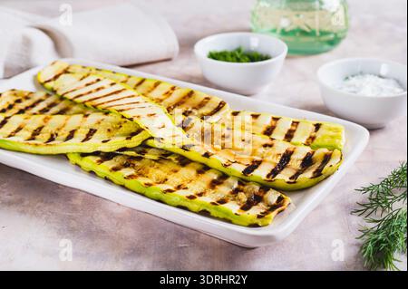 Fette di zucchine grigliate su un piatto con salsa ed erbe sul tavolo Foto Stock