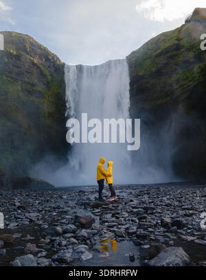 Una coppia si trova mano nella mano alla base della cascata Skogafoss in Islanda. Foto Stock