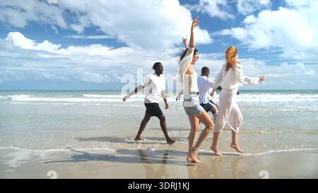 Gruppo di amici diversi che si divertono in spiaggia, camminano e nuotano tra le onde Foto Stock