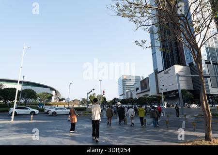 Persone che camminano sul marciapiede urbano vicino ai moderni grattacieli e allo stadio ricurvo sotto il cielo limpido Foto Stock