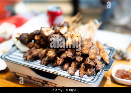 Spiedini grigliati con funghi e piatti di carne su metallo, cucina asiatica di strada, ambiente da pranzo all'aperto Foto Stock