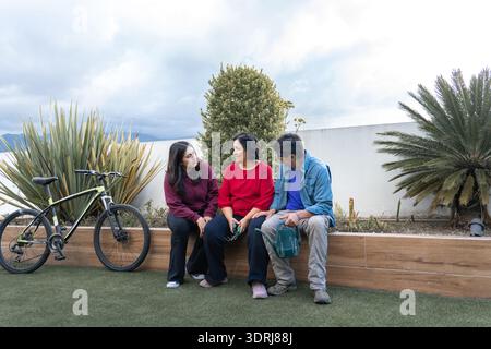 I membri della famiglia seduti e conversano all'aperto su un patio con una bicicletta Foto Stock