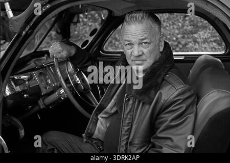Ritratto in bianco e nero un uomo anziano con un soffio seduto al posto di guida di un'auto d'epoca, con una giacca di pelle nera. Foto Stock