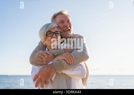 Coppie anziane che si abbracciano godendosi le attività ricreative all'aperto a piedi sulla spiaggia. Vecchio marito moglie che abbraccia con tenerezza amore godere Foto Stock