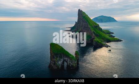 Maestose formazioni rocciose sorgono dalle acque tranquille delle Isole Faroe al crepuscolo Foto Stock
