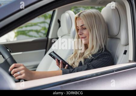 Donna imprudente che guida un'auto mentre guarda uno smartphone e invia SMS. Foto Stock