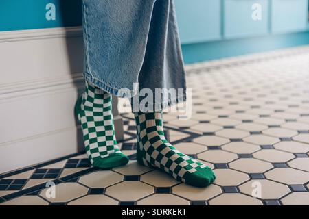 Gli individui che indossano calze a scacchi verdi e bianche si stagliano su pavimento piastrellato a motivi geometrici, mostrando moda e comfort casual in una st Foto Stock