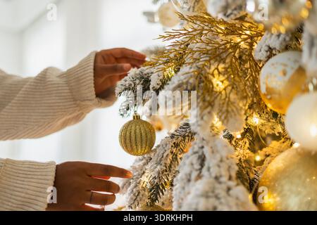 Buon Natale. Donna afroamericana che decora l'albero di Natale. Ragazza vicino al classico albero di Natale con bianco dorato si Foto Stock