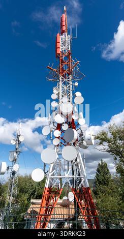 Vista ad angolo basso di una torre di telecomunicazioni rossa e bianca con più antenne e apparecchiature, fotografata sotto un cielo blu brillante in Andalus Foto Stock