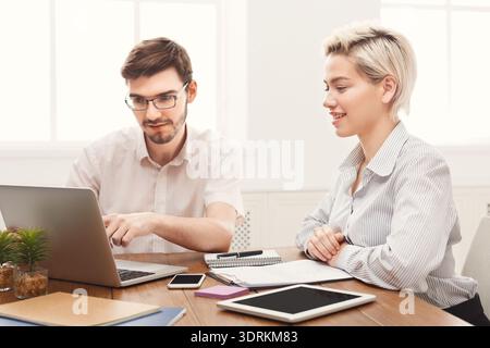 Due persone che lavorano insieme a un tavolo con dispositivi durante la giornata Foto Stock