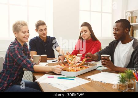 Gli amici si riuniscono per gustare pizza e bevande mentre lavorano a progetti in Cozy Space Foto Stock