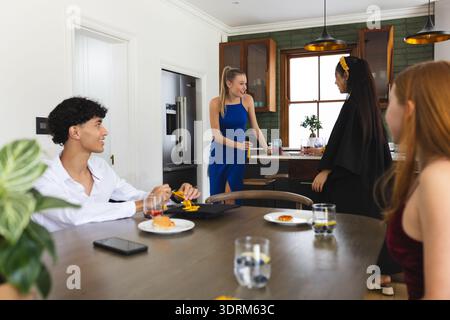 Gli adolescenti festeggiano a casa, gustando spuntini e chiacchierando in cucina. Adolescenti, festa, riunione, casual, legame, all'interno Foto Stock