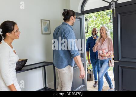 Accogliere gli ospiti a casa, sorridere coppie che salutano gli amici all'ingresso. Ospitalità, amicizia, riunione, arrivo, interazione, Foto Stock