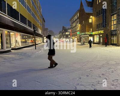 Strada innevata a Tromso, Norvegia all'ora blu con pedoni e vetrine illuminate durante le nevicate invernali. Foto Stock