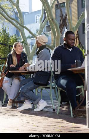Coppia che ride e si piega, tenendosi per mano nel patio della caffetteria sul lato della strada con un computer portatile nelle vicinanze Foto Stock