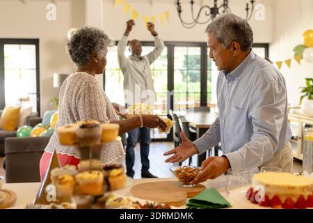 Coppia senior che si gode una riunione festosa con spuntini e decorazioni a casa. Celebrazione, anziani, festa, cibo, stile di vita, happ Foto Stock