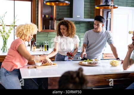 Diversi amici preparano spuntini insieme nella cucina moderna, godendosi una conversazione informale. Cucina, cucina, amicizia, casa, Foto Stock