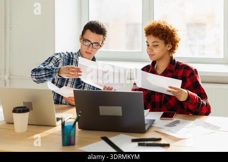 Brainstorming sul lavoro di squadra. Diversi colleghi che lavorano insieme discutono le statistiche finanziarie. Gruppo di giovani felici e moderni sittin Foto Stock