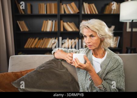 Buon mattino autunno inverno atmosfera autunnale. Confortevole anziana anziana rilassata che beve bevande calde tè e caffè nel divano di casa. Foto Stock
