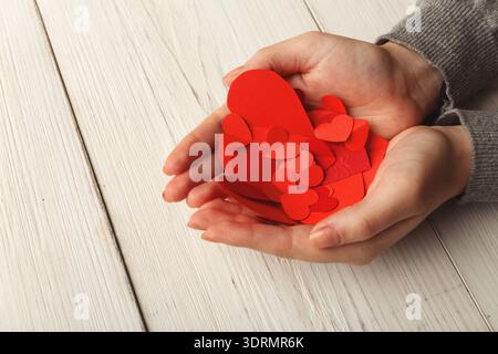 Collezione di forme a cuore rosso tenute in mano su un tavolo di legno Foto Stock