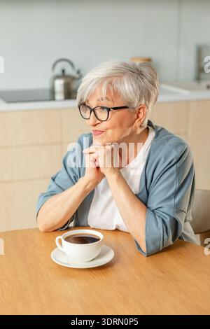 Buon giorno. Comfort rilassato anziano anziano anziano anziano donna nonna che beve bevande calde tè e caffè in cucina a casa. Maturo W Foto Stock