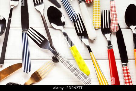 Set di posate colorate disposte su una superficie in legno bianco con un design piatto Foto Stock