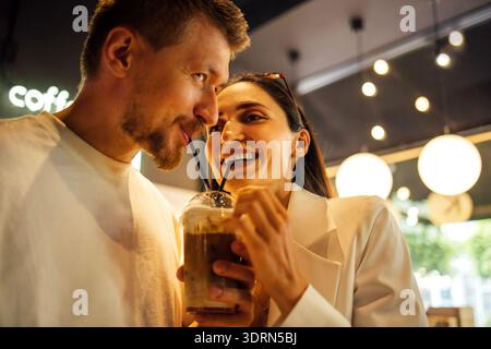 Coppia che si gusta un caffè insieme in un accogliente caffè, condividendo sorrisi e risate, circondati da una calda illuminazione e da un'atmosfera rilassata Foto Stock