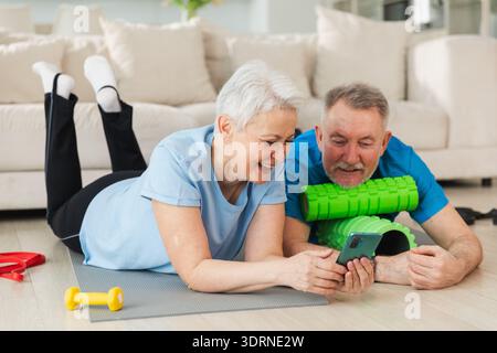 Yoga fitness training online. Coppia senior che pratica yoga fitness con lezioni online su smartphone. Vecchia moglie marito che guarda Foto Stock