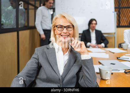 Ritratto di donna in ufficio, donna d'affari del team leader, riunione di colleghi in background. Donna leader d'affari sorridente e sicura di sé Foto Stock