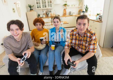 Festa in casa. Allegro gruppo di amici che giocano ai videogiochi a casa. Amici di gruppo felici e diversi che si divertono insieme al chiuso. Frien Foto Stock