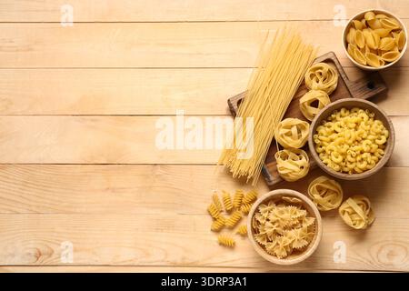 Tagliere e ciotole con diversi tipi di pasta cruda su fondo in legno Foto Stock