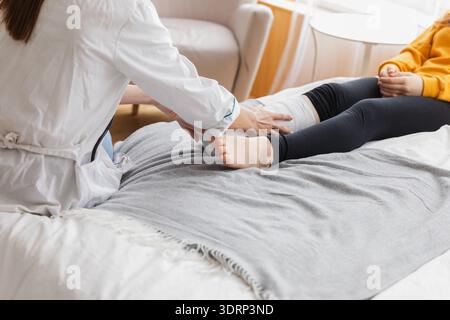 Ragazza con gamba rotta e medico in clinica, Traumatologo ortopedico esamina gamba bambino in studio medico. Medico che esamina il gir Foto Stock