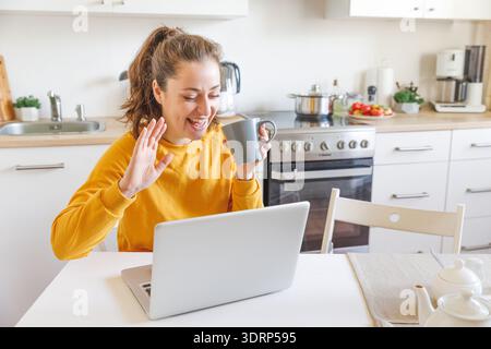 Ragazza sorridente che salta la mano videochiama la famiglia con la webcam. Donna con laptop che ha una riunione virtuale in videoconferenza Foto Stock