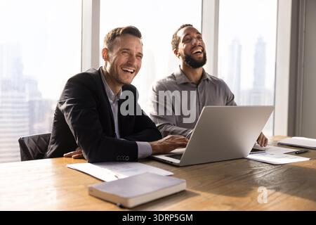 Due allegri uomini d'affari multietnici che lavorano insieme al computer portatile Foto Stock