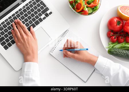 Nutrizionista donna che lavora con notebook e notebook sul tavolo, vista dall'alto Foto Stock
