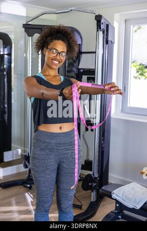 Donna afroamericana di 29 anni in abbigliamento sportivo in piedi in palestra con metro rosa. Fitness, salute, benessere, esercizio, forza, motivati Foto Stock