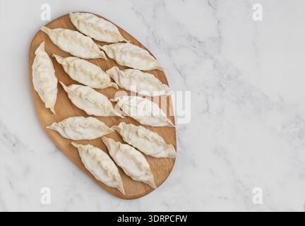 Gyoza crudi su un asse di legno. Messa a fuoco selettiva, vista dall'alto Foto Stock