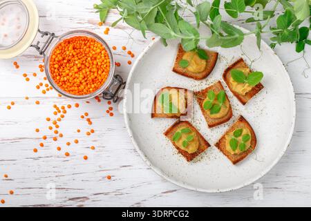 Delizioso pane tostato con hummus (paté, pasta, salsa) di lenticchie e carote con germogli di pisello su un piatto bianco. Colazione salutare Foto Stock