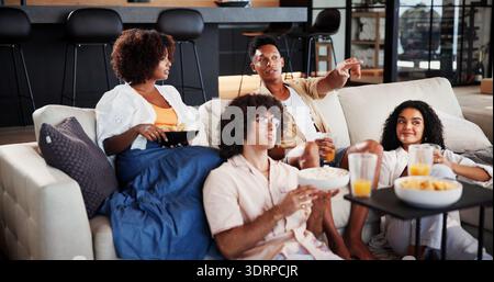 Coppia di amici, emozionati e rilassati guardando la tv sul divano per una partita sportiva, un punto o uno spuntino nel soggiorno. Gente, felice e beve sul divano per Foto Stock