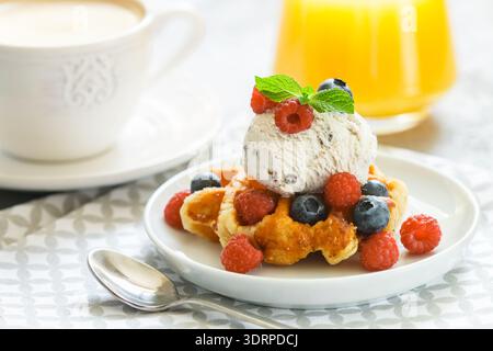 Waffle fatti in casa con gelato e frutti di bosco freschi, lamponi e mirtilli. Delizioso dessert, cappuccino e succo d'arancia Foto Stock