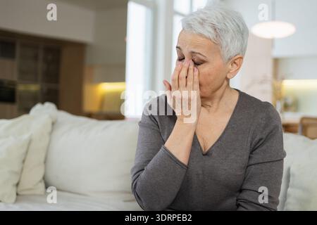 Triste stanca malata malata solitaria delusa anziana donna seduta a casa da sola. Infelice nonna matura che soffre di dolore Foto Stock