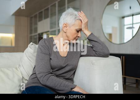 Triste stanca malata malata solitaria delusa anziana donna seduta a casa da sola. Infelice nonna matura che soffre di dolore Foto Stock