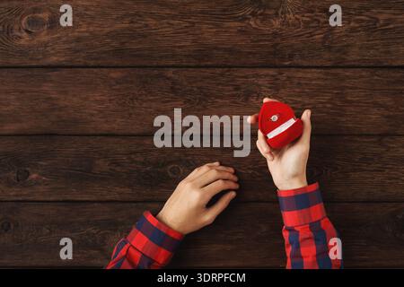 La persona tiene la scatola ad anello rossa su un tavolo di legno per una proposta o un regalo a sorpresa Foto Stock