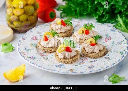 Mousse di salmone affumicato (trota), formaggio cremoso (ricotta) con olive, peperoni e lattuga su un pane scuro con semi. mini Foto Stock