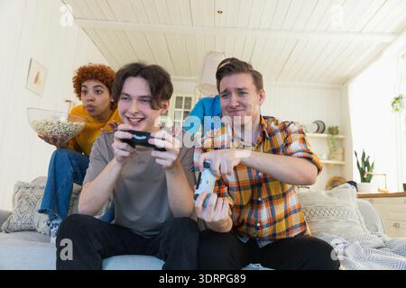 Festa in casa. Allegro gruppo di amici che giocano ai videogiochi a casa. Amici di gruppo felici e diversi che si divertono insieme al chiuso. Frien Foto Stock