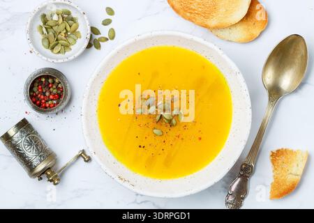 Crema vegetariana dietetica purea di zucca, carote e patate con olio d'oliva, semi e spezie su un tavolo di marmo bianco Foto Stock
