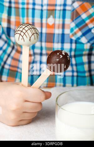 Due pop torta decorata con il bianco e il cioccolato fondente in bambini con le mani in mano. Dessert per piccoli buongustai. Messa a fuoco selettiva Foto Stock