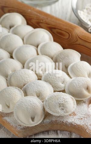 Processo di preparazione di gnocchi di pasta cruda fatti in casa con ripieno di carne su un bordo di legno. Pelmeni. Un piatto tradizionale di cuis russi Foto Stock