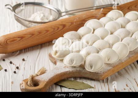 Processo di preparazione di gnocchi di pasta cruda fatti in casa con ripieno di carne su un bordo di legno. Pelmeni. Un piatto tradizionale di cuis russi Foto Stock